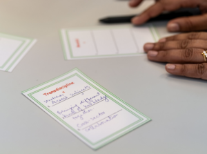 Photo of hands holding a pen with a card on a table that reads "Transdiciplinary" 