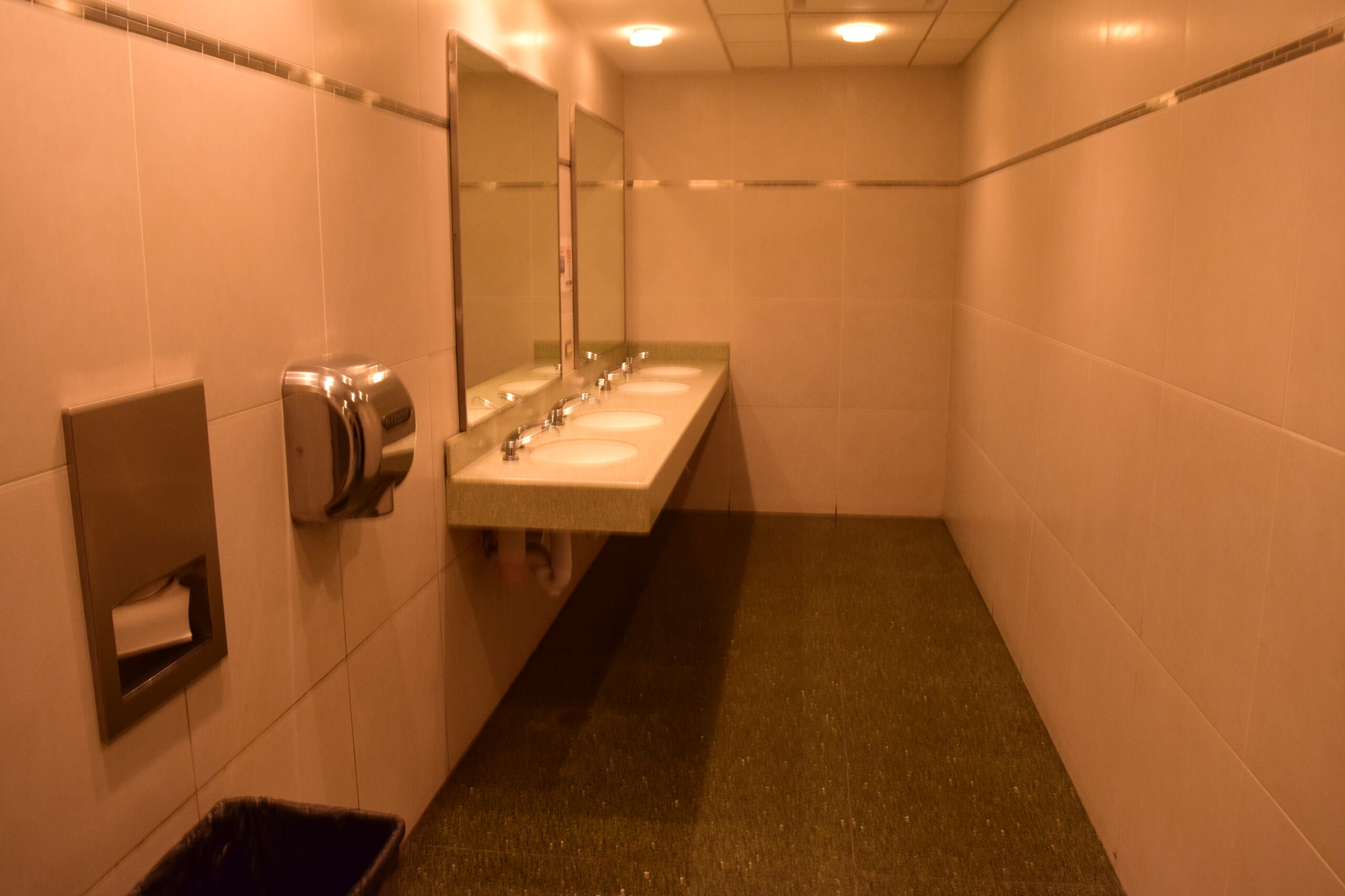 A row of sinks, with a paper towel dispenser and automatic air hand dryer to the left.