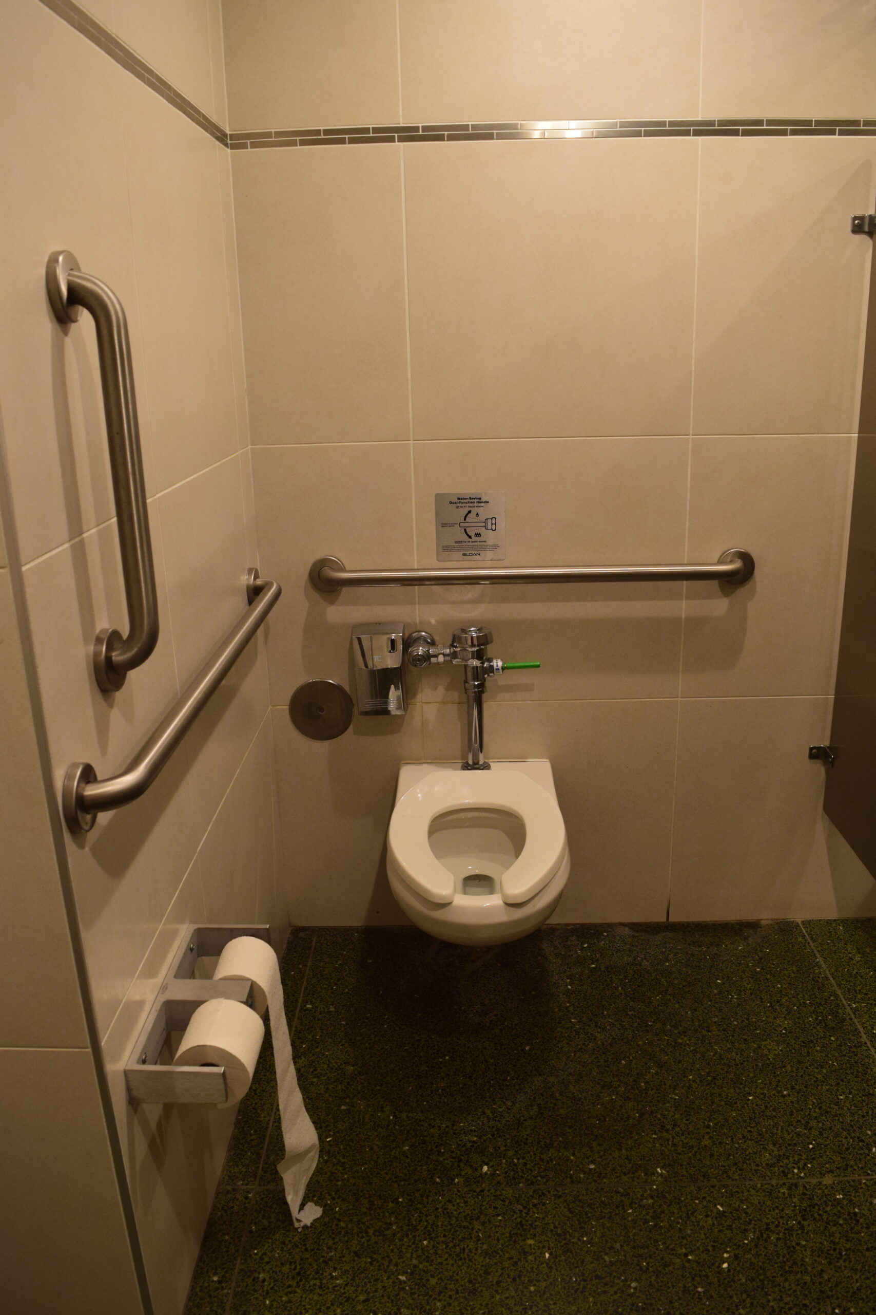 A toilet with grab bars on the right and behind, and two toilet paper dispensers in front and on the right of the toilet.